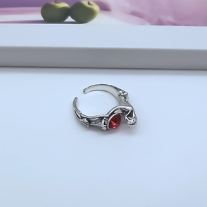 Detail of a punk style open ring with red teardrop gemstone and engraved silver alloy wings