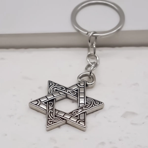 Silver hexagram star keychain with celtic knot engravings on a white stone background