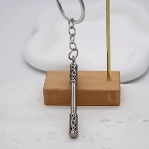 Polished silver metal staff keychain with intricate hollow cloud patterns on a wooden stand