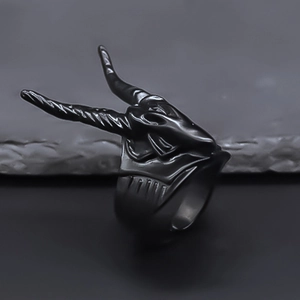 Macro view of a punk style black goat head ring with long spiral horns on stone surface