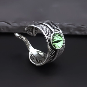 Macro detail of retro feather ring featuring a vibrant green eye on textured stone