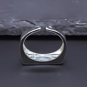 Detailed view of silver geometric ring with flat top surface on a grey mineral background