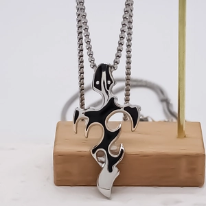 Polished alloy distorted cross necklace with tribal flame patterns on a wooden stand