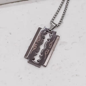 Close-up of razor blade pendant with intricate engraved floral pattern on steel chain