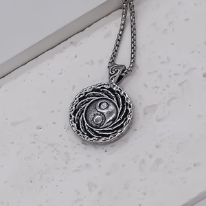 Détail macro du pendentif Tai Chi Yin Yang en acier oxydé avec une chaîne maille boîte