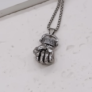 Macro shot of silver fist pendant with geometric details and box chain on white stone