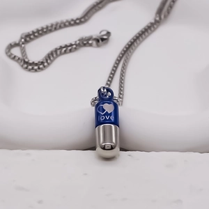 Gros plan du pendentif capsule bleu et argent avec gravure de cœur sur la chaîne