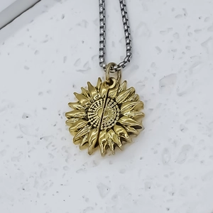 Gros plan du pendentif tournesol doré avec pétales ciselés sur chaîne box en argent