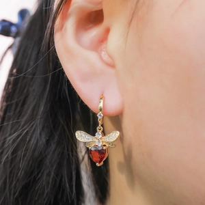 Exquisite gold bee drop earrings with red heart gemstone and diamond accents on model
