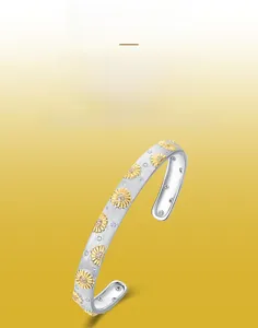 Macro view of brushed S925 silver cuff bracelet featuring gold daisy floral engravings