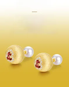 Detail of handmade brushed gold earrings with red garnet stones and pearl backings