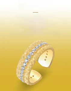 Dettaglio macro di anello dorato con motivo a rombi, finitura spazzolata e cristallo