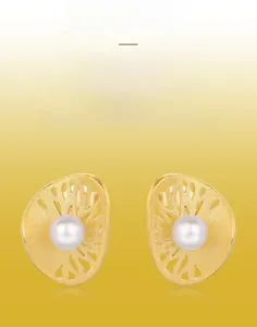 Detail of handmade brushed gold earrings featuring a radiant leaf design and central pearl