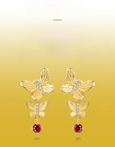 Detail of gold butterfly earrings with brushed texture, zircons and red faceted gemstone