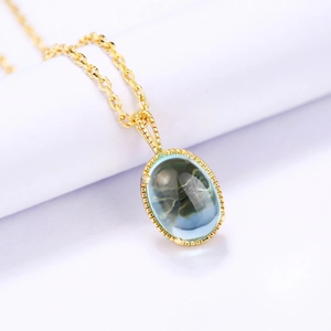 Vue macro détaillée du pendentif en cristal bleu-vert ovale sur une chaîne dorée