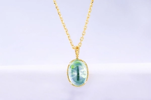 Détail d'un pendentif ovale en cristal vert sur chaîne dorée avec effet œil-de-chat
