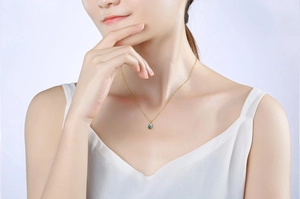 Gros plan d'un collier en chaîne dorée avec pendentif ovale en pierre verte sur la peau