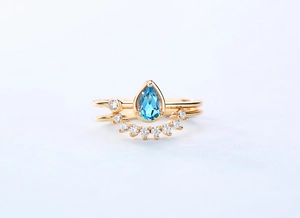 Macro detail of pear-shaped blue topaz ring with gold band and sparkling accents