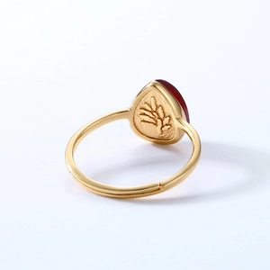 Golden open ring with teardrop garnet stone and leaf carving on white background