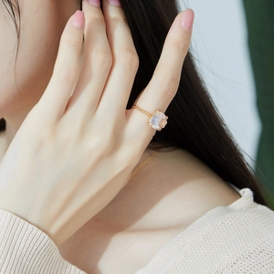 Detail of a gold beaded ring featuring a square rose quartz stone on a model's finger