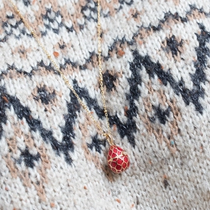Macro detail of red enamel egg pendant with gold lattice on a knitted sweater background