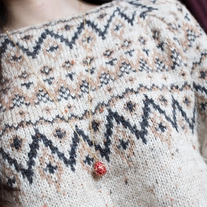 Close-up of a 9K gold-plated red egg pendant necklace worn over a white sweater