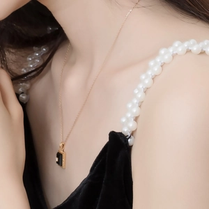 Macro detail of rectangle black agate pendant on gold chain worn by a female model