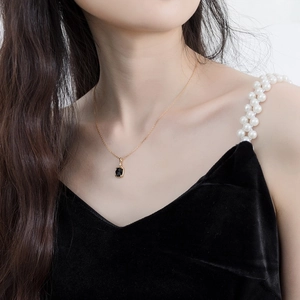Close-up van een vergulde zilveren ketting met een vierkante zwarte agaat hanger op een model