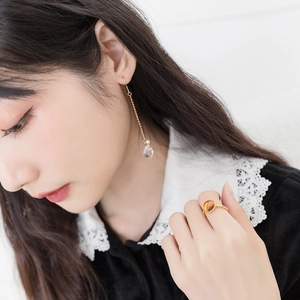 Detail of amber gemstone ring and long gold chain earring worn by a model