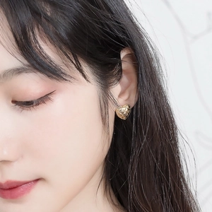Close-up of heart-shaped gold stud earring with detailed quilted pattern on earlobe