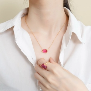 Elegant gold necklace and ring set with red geometric gemstones on a white shirt