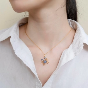 Détail macro du pendentif crabe doré avec zircons bleus porté par un mannequin féminin