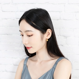 Detail of geometric rhombus gold earrings with textured finish worn by a model