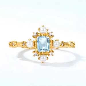 Anello geometrico con topazio blu e perle in finitura oro vintage su sfondo bianco