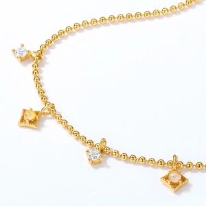 Dettaglio di bracciale a sfere dorate con pendenti in opale e pietre di zircone