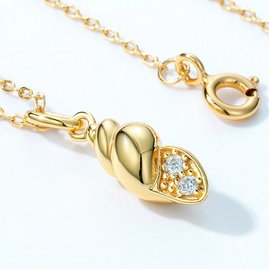 Macro detail of gold-plated conch shell pendant featuring clear cubic zirconia accents