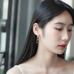 Detail of a long gold linear earring with delicate chain and white round bead on model