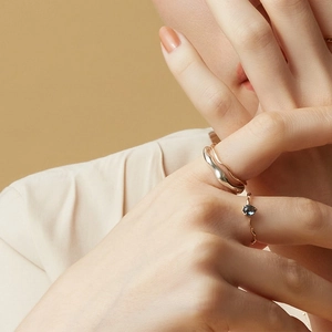 Close-up of wavy gold ring set and pear-cut blue gemstone on model's hand