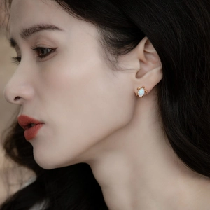Close-up of a model wearing a gold sea turtle stud earring with white opal inlay