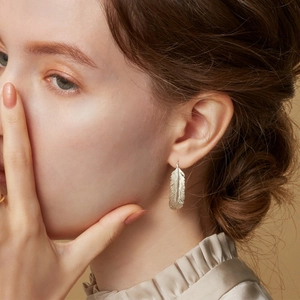 Elegant S925 sterling silver feather drop earrings worn by a model in soft studio lighting