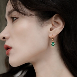 Detailed close-up of a gold Hamsa hand earring with green malachite inlay on model