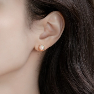 Détail de puce d'oreille opale ronde avec bord perlé doré sur l'oreille du mannequin