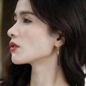 Close-up of long gold tassel earrings with black zircon stones worn by a model