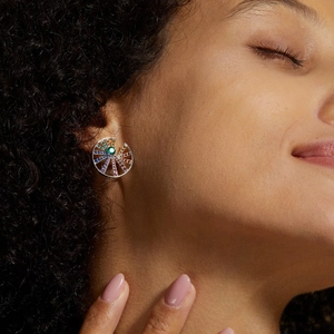 Detail view of rainbow pinwheel earring with colorful gemstones on woman earlobe