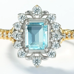 Macro view of emerald-cut blue topaz ring with diamond floral halo and gold braided band