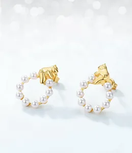 Detailed close-up of golden bear stud earrings with white shell pearls in soft focus