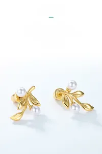 Detail of leaf-shaped gold stud earrings with white shell pearls on white background