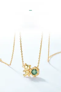 Close-up of golden bear necklace with a hexagonal green moss stone pendant on light blue