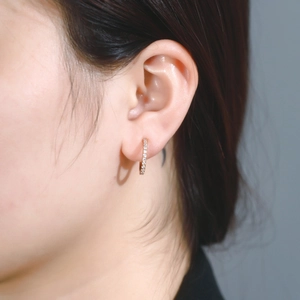 Close-up of small gold huggie earrings with pave setting sparkling stones on a model