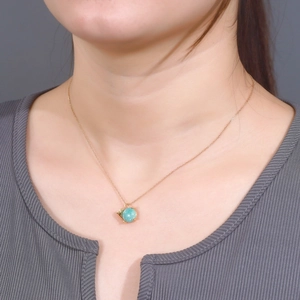 Close-up of a gold necklace featuring a light blue amazonite sphere pendant on a model